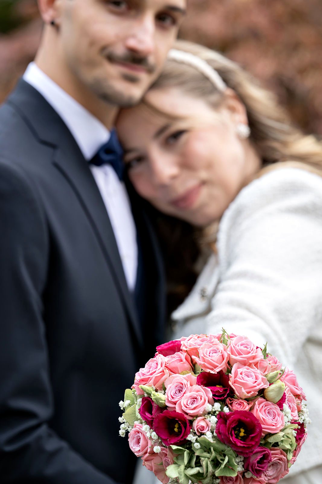 Brautstrauss mit rosa Rosen scharf im Vordergrund, das Brautpaar unscharf dahinter