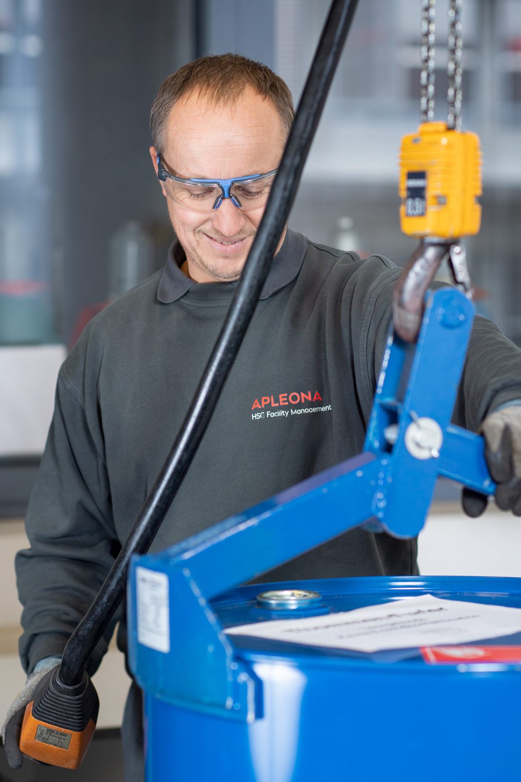 Fachmann mit Schutzbrille hebt ein Fass mit dem Kettenzug an – Handwerk-Content Region Basel