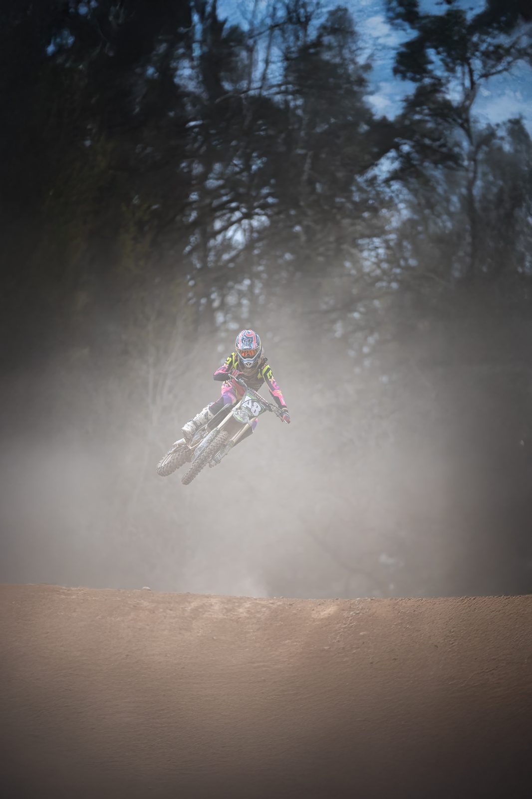 Motocross-Fahrer im Sprung, hinter ihm eine Staubwolke