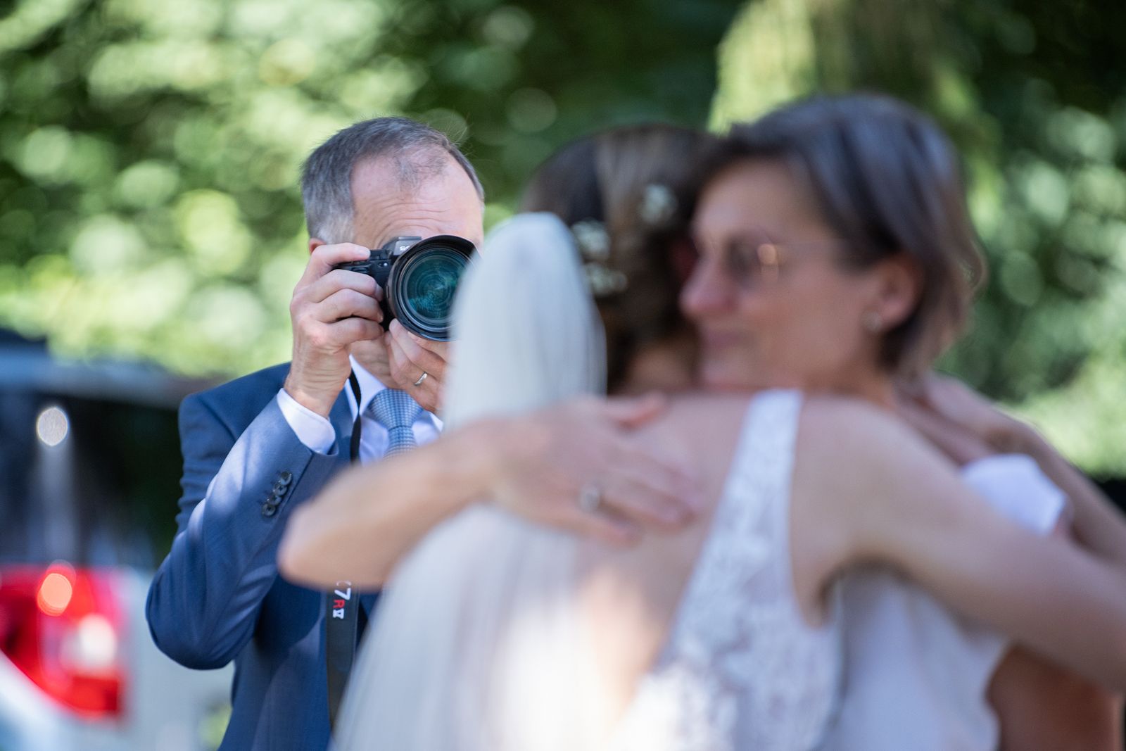 Braut umarmt eine Gratulantin, im Hintergrund fotografiert ein Gast